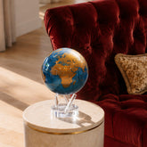Cerulean Blue & Gold MOVA Globe on base styled beside a velvet armchair in a modern luxury interior.