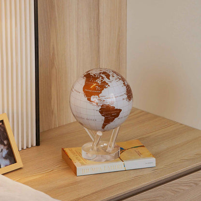 Pearl White &amp; Gold MOVA Globe displayed on books in a modern wood shelving unit